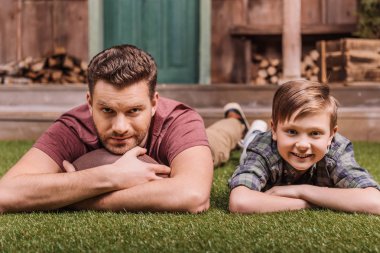 father with son laying on grass clipart