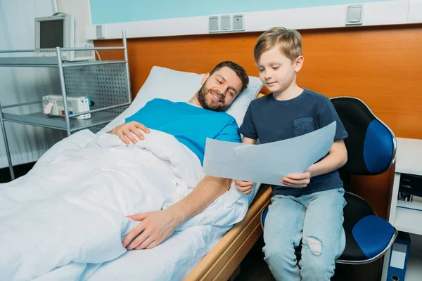 Сын показывает больного отца рисунки — стоковое фото