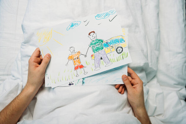 father holding drawings while laying at ward