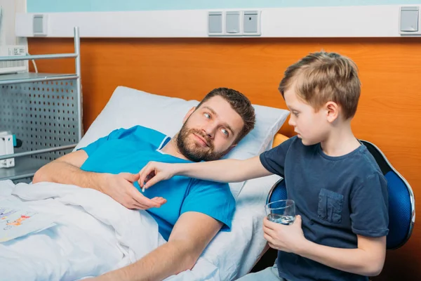 Filho dando pílulas para o pai doente — Fotografia de Stock