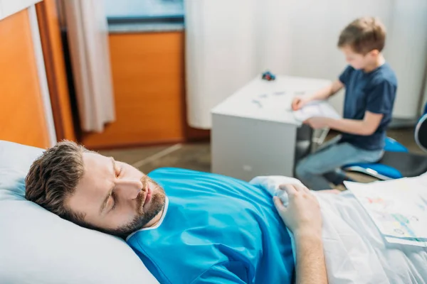 Son drawing while sick father laying — Stock Photo, Image