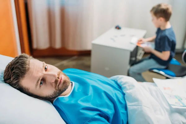 Son drawing while sick father laying — Stock Photo, Image