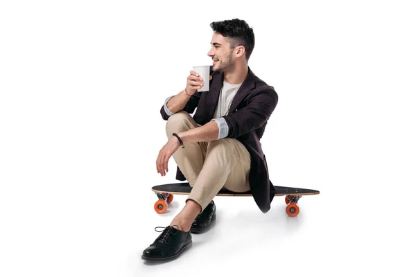 Человек пьет напиток, сидя на скейтборде — стоковое фото