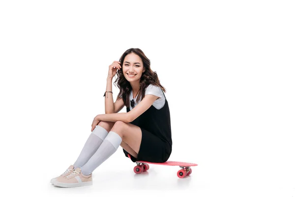 Улыбающаяся азиатская девушка сидит на скейтборде — стоковое фото