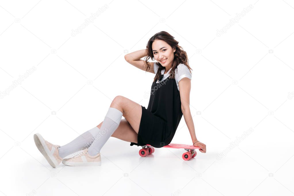smiling asian girl sitting on skateboard