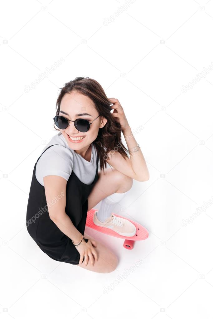 smiling woman in sunglasses sitting on skateboard
