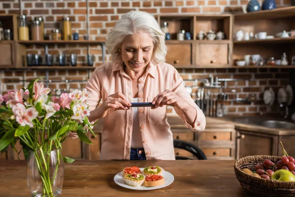 Mujer fotografiando plato con comida en la cocina — Foto de Stock