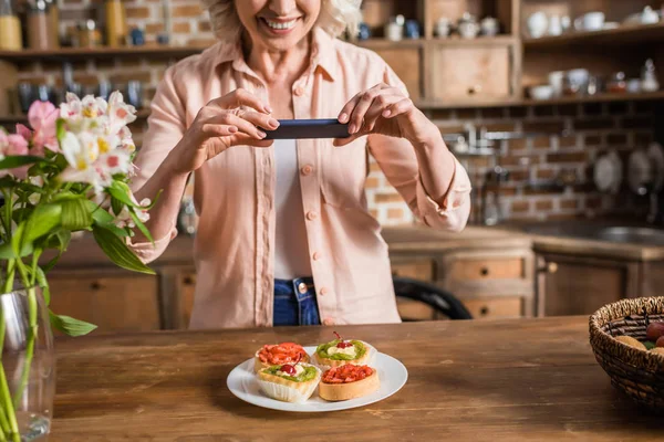 Mujer fotografiando plato con comida en la cocina — Foto de Stock
