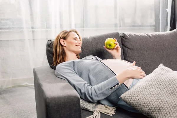 Těhotná žena odpočívá na šedé rozkládací — Stock fotografie