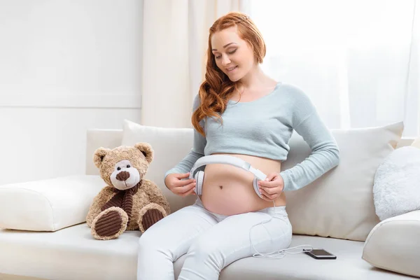 Těhotná žena se sluchátky na břicho — Stock fotografie