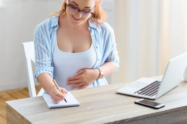 Pregnant woman writing in notepad — Stock Photo, Image