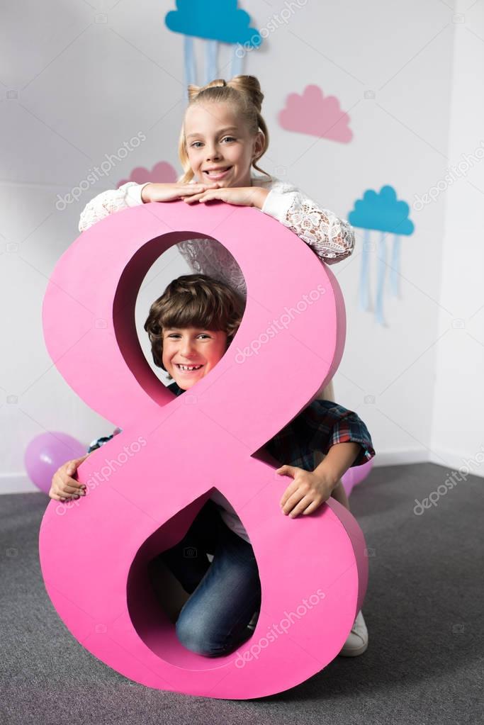 Adorable happy kids posing with decorative pink number eight at birthday party