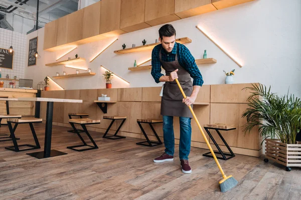 Worker cleaning floor with sweep — Stock Photo, Image