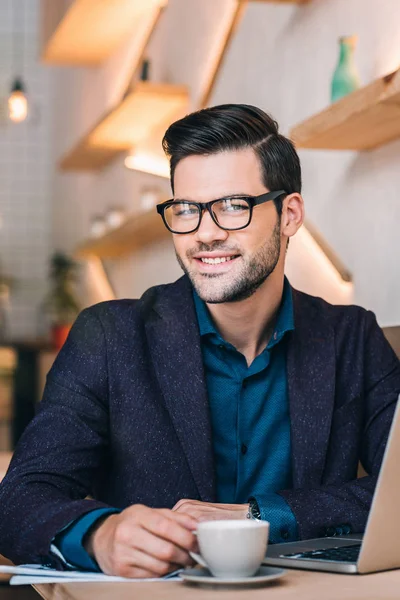 Hombre de negocios sonriente con portátil en la cafetería —  Fotos de Stock