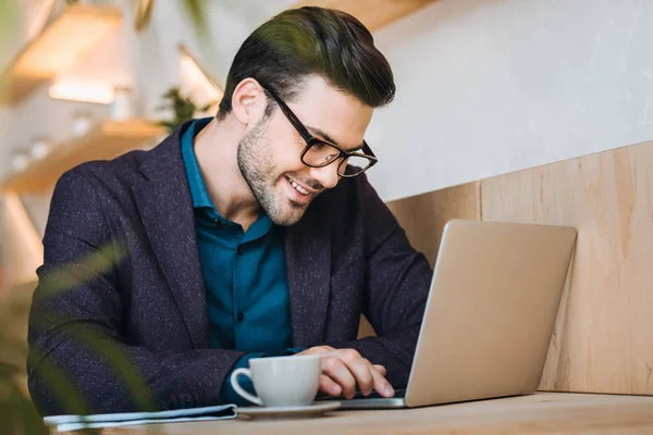 Hombre de negocios sonriente con portátil en la cafetería — Foto de Stock