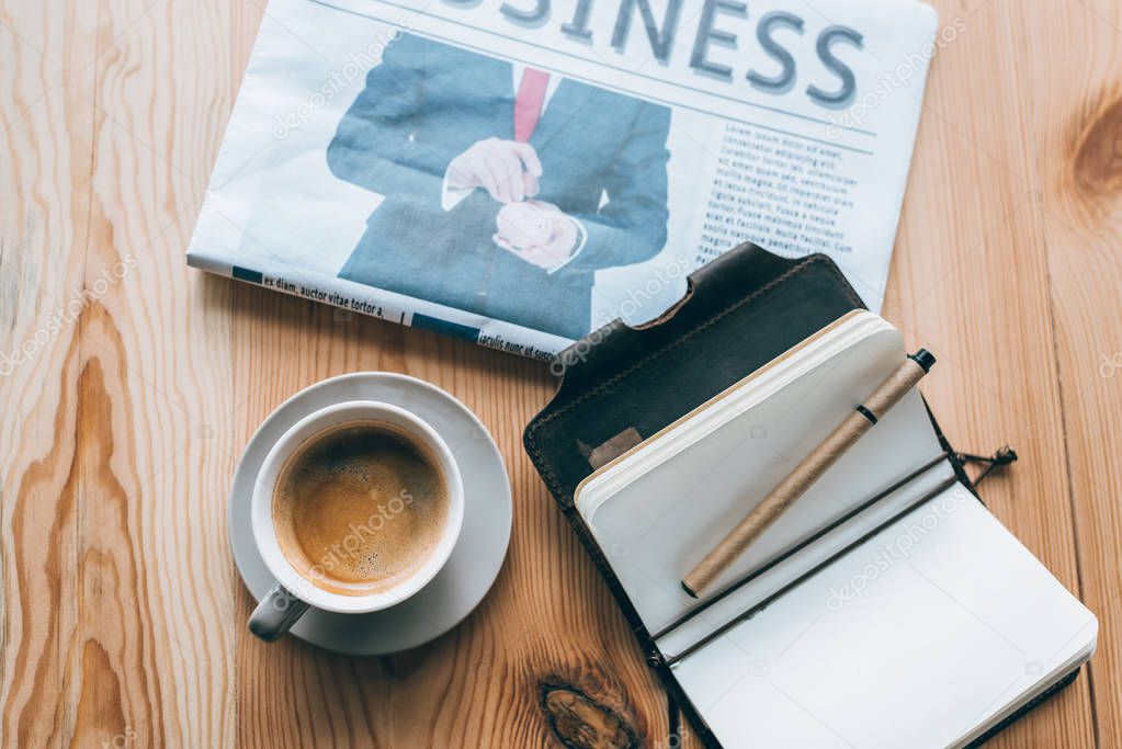 cup of coffee, newspaper and notebook on table