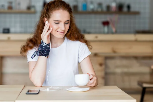 Girl in earphones drinking coffee — Free Stock Photo