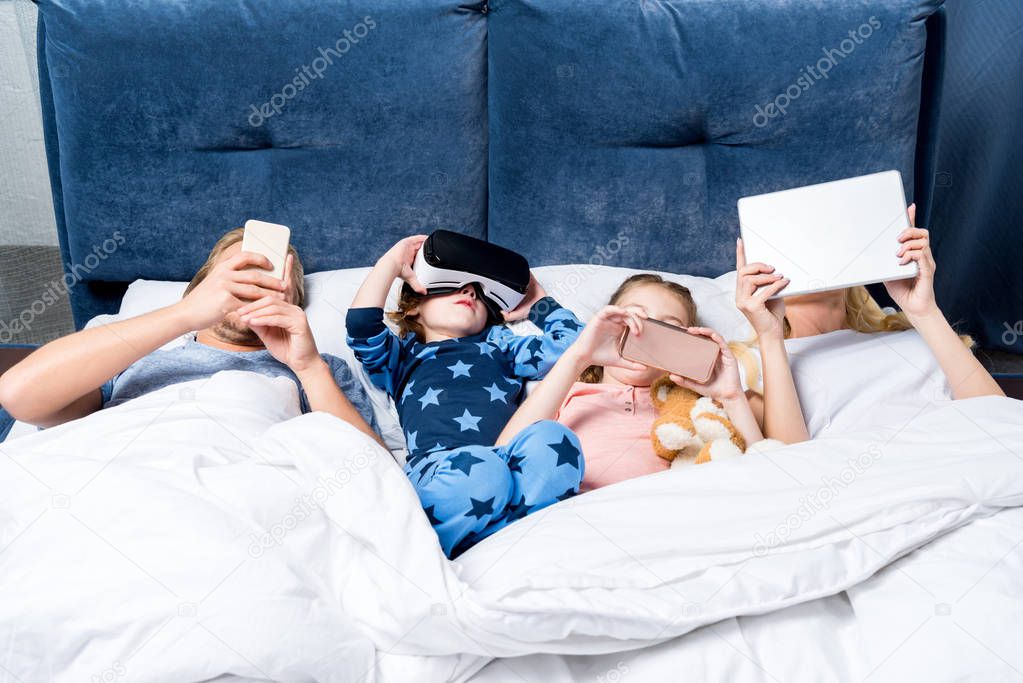 family with gadgets in bed