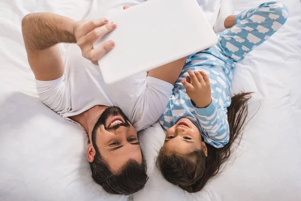 Отец и дочь с помощью планшета в постели — стоковое фото