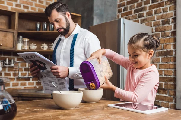 Filha derramando cereal em tigela para o pai — Fotografia de Stock