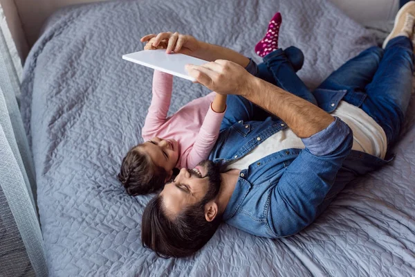 Батько і дочка використовують планшет у ліжку — стокове фото