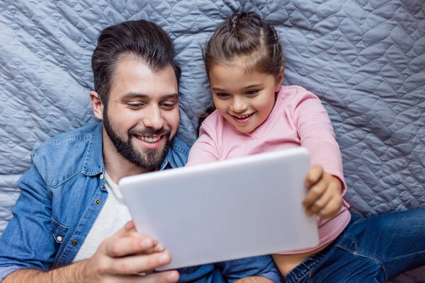 father and daughter using tablet in bed