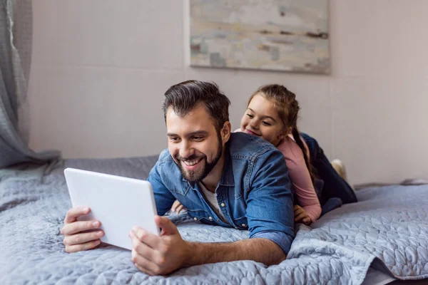 Far och dotter använder surfplatta i sängen — Stockfoto