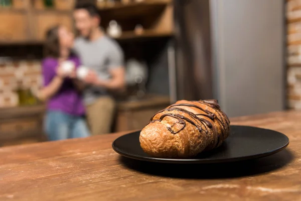 夫妇与咖啡在厨房 板材与牛角面包在前景 — 图库照片