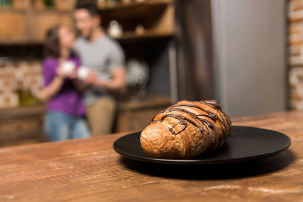 couple with coffee in kitchen, plate with croissant on foreground