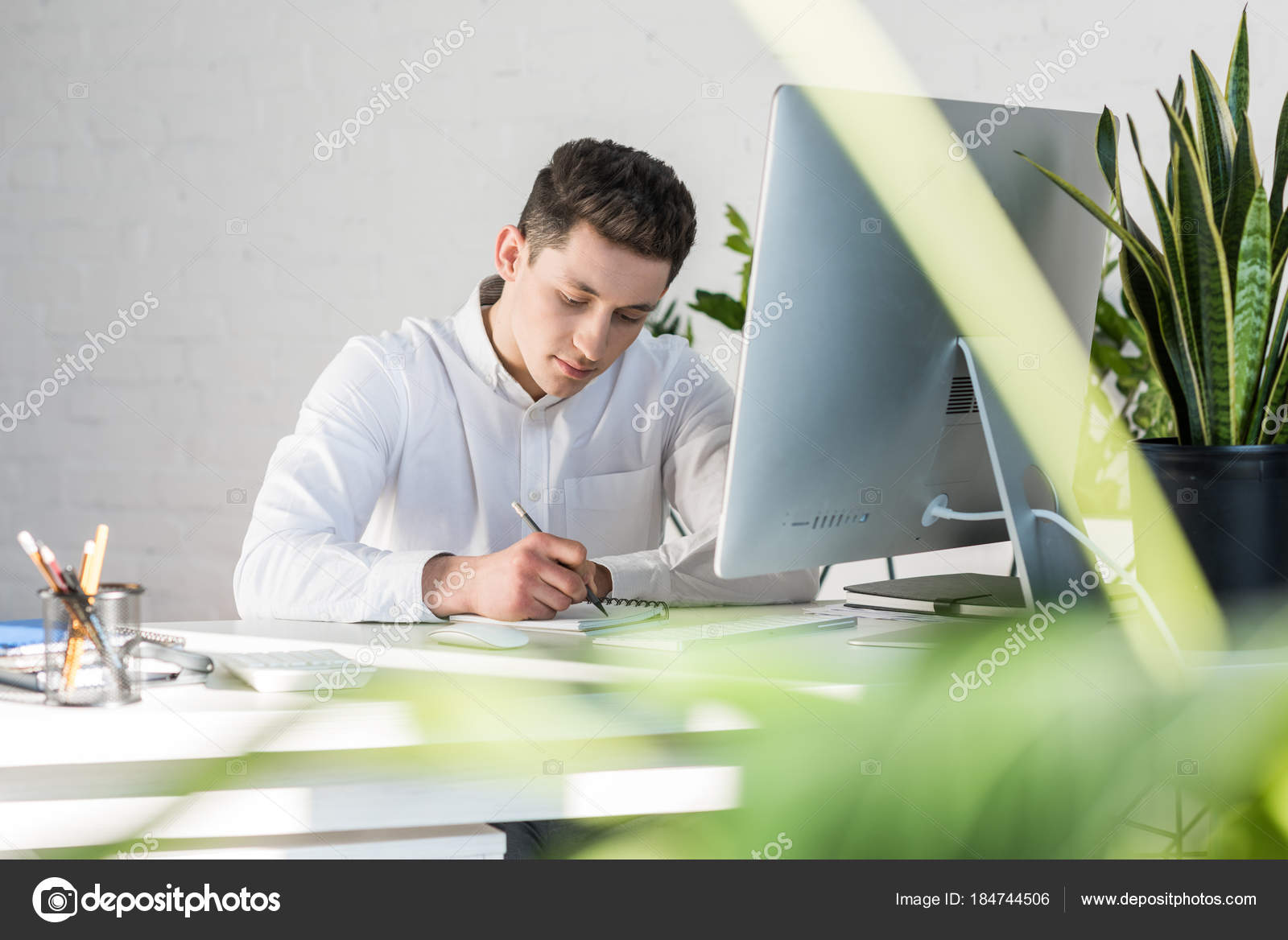 Focused young businessman writing notes at workplace