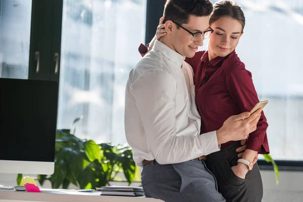 Τους Συναδέλφους Αγκαλιάζοντας Και Χρησιμοποιώντας Smartphone Μαζί Στο Γραφείο — Φωτογραφία Αρχείου
