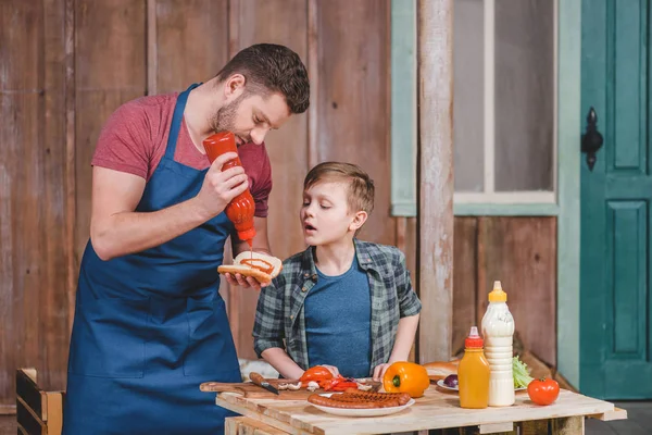 Padre e hijo cocinando hot dog - foto de stock