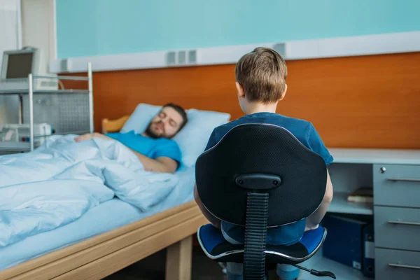 Hijo sentado cerca de padre enfermo en la sala - foto de stock