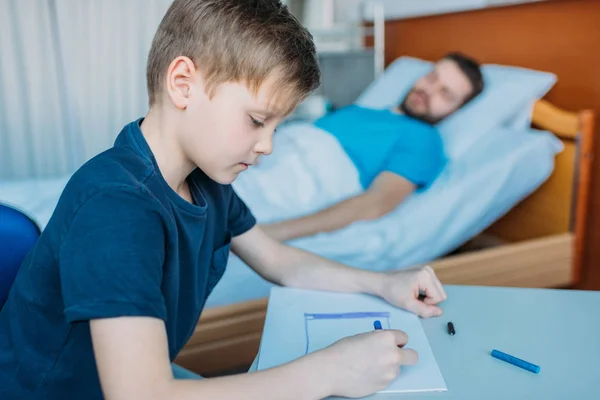 Сын рисует, пока больной отец лежит — стоковое фото