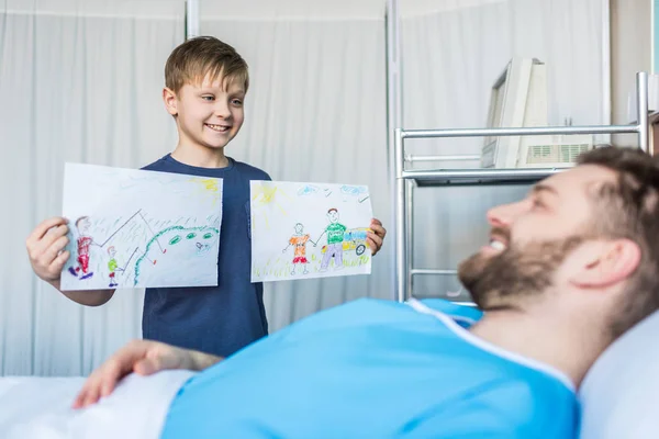 Figlio mostrando disegni padre malato — Foto stock