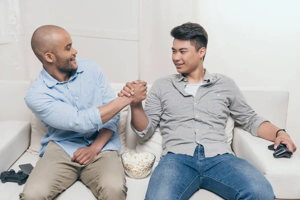 Amigos multiétnicos handshaking enquanto sentado em casa — Fotografia de Stock