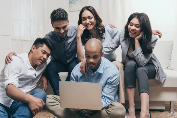 Amigos multiétnicos mirando a la computadora portátil en casa - foto de stock