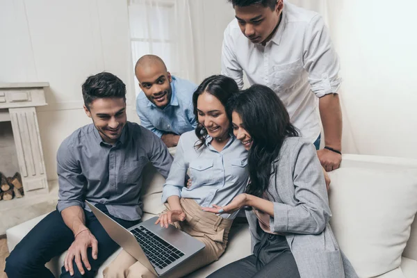 Amigos sonrientes usando el ordenador portátil en casa - foto de stock