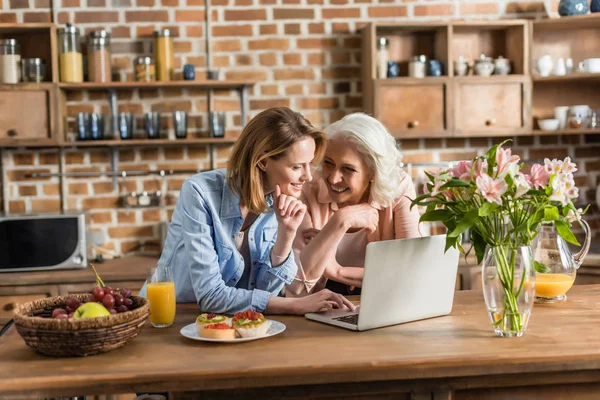 Mujeres usando el ordenador portátil en la cocina - foto de stock
