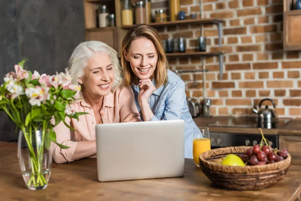 Mujeres usando el ordenador portátil en la cocina - foto de stock