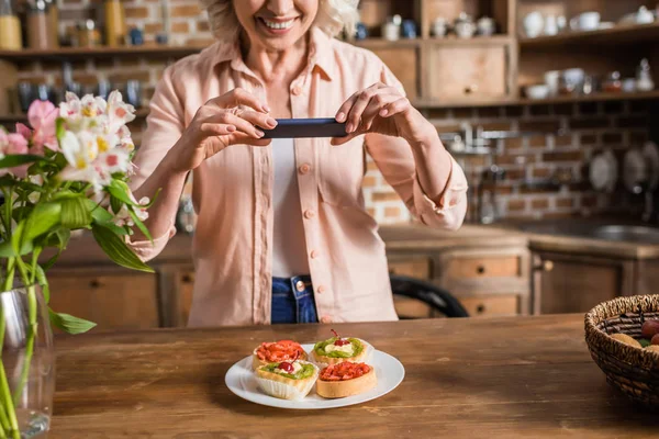 Femme photographier plaque avec de la nourriture à la cuisine — Photo de stock