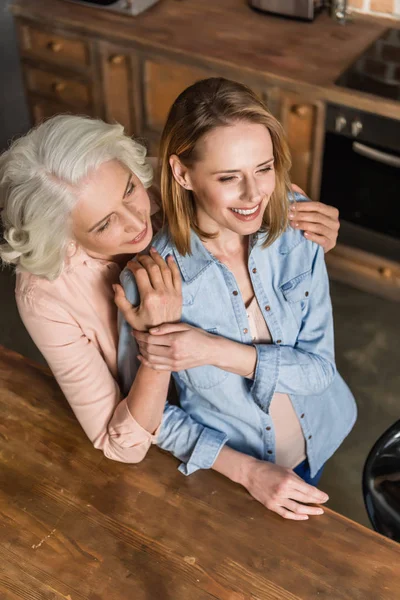 Dos mujeres abrazándose en la cocina - foto de stock