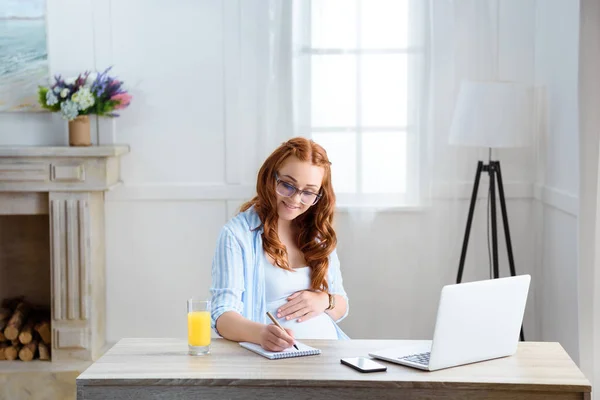 Pregnant woman writing in notepad — Stock Photo