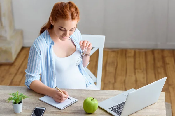 Pregnant woman writing in notepad — Stock Photo