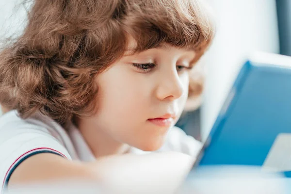 Thoughtful curly kid using tablet — Stock Photo