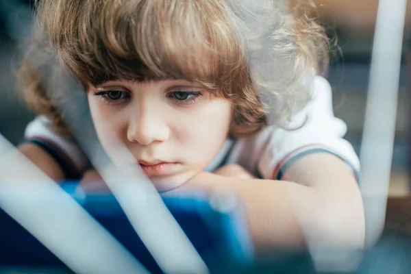 Thoughtful curly kid using tablet — Stock Photo