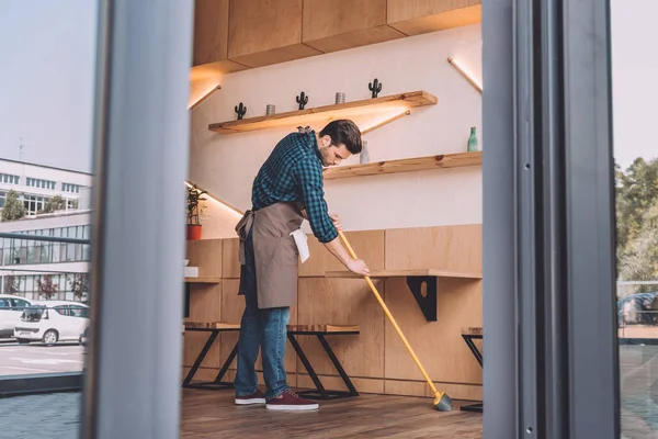 Worker cleaning floor with sweep — Stock Photo