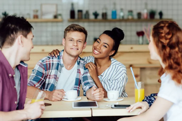 Pareja multiétnica con amigos en la cafetería - foto de stock