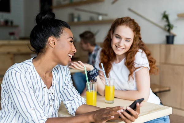 Meninas multiétnicas com smartphone e suco — Fotografia de Stock