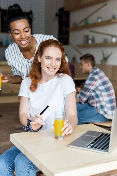 Multiethnic girls with juice and credit card — Stock Photo